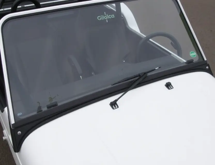 A close-up shot of a Caterham Seven 270 with a replaced windshield. The windshield is clear and new, contrasting with the older, slightly damaged windshield that has been removed. The car is parked on a clean, paved surface. Focus on the details of the replacement process and the quality of the new windshield.