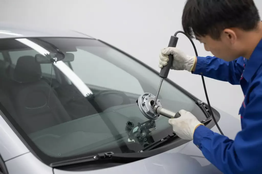 A professional mechanic in a clean workshop carefully installing a new windshield into a modern Acura sedan, using specialized tools, bright lighting, high detail