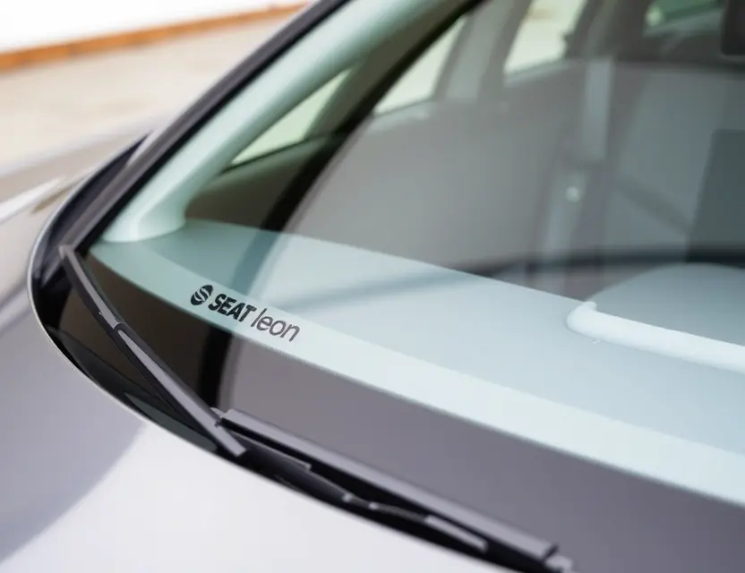A close-up shot of a SEAT Leon with a replaced windshield. The new windshield is clear and seamless, integrating with the car's design. Focus on the quality of the replacement and the modern aesthetic.
