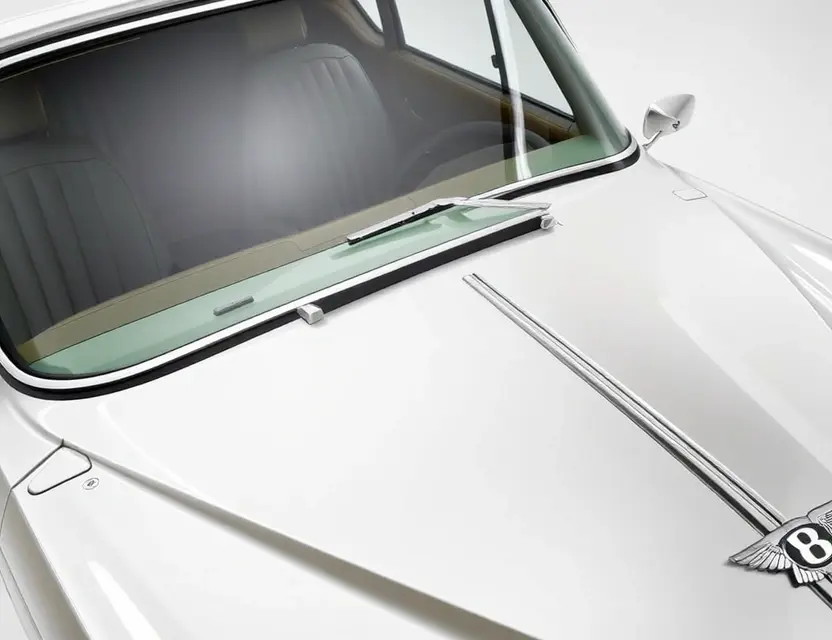 A high-quality image depicting a Bentley T1 with a replaced windshield. The windshield is clear and new, seamlessly integrated with the existing frame. The car is parked on a clean, well-lit surface, possibly a showroom or garage. Focus on the detail of the replacement and the car's overall condition.