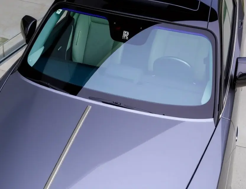 A Rolls-Royce Spectre with a replaced windshield, showcasing the new glass. The car is parked on a clean, modern surface. Focus on the clarity and quality of the replacement windshield.