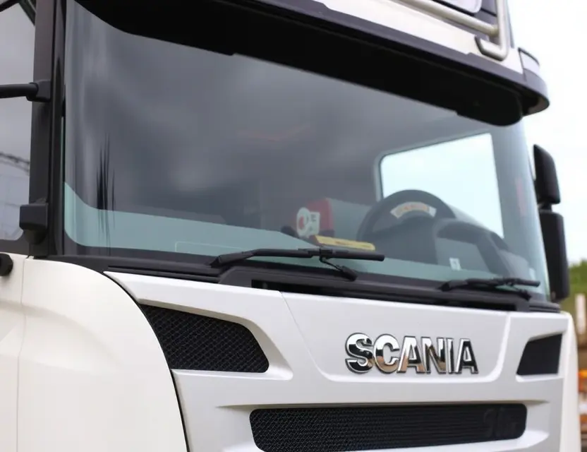 A close-up shot of a Scania R-series V8 truck with a replaced windshield. The windshield is clear and new, contrasting with the older, replaced section. Focus on the details of the replacement process and the truck's robust design.