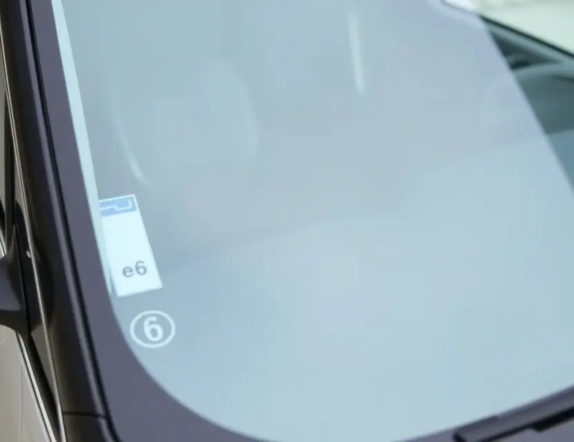 A close-up shot of a BYD e6 electric vehicle with a replaced windshield. The new windshield is seamlessly integrated with the old one, showing a clear, modern design. The car is parked on a clean, well-lit surface. Focus on the windshield replacement detail.