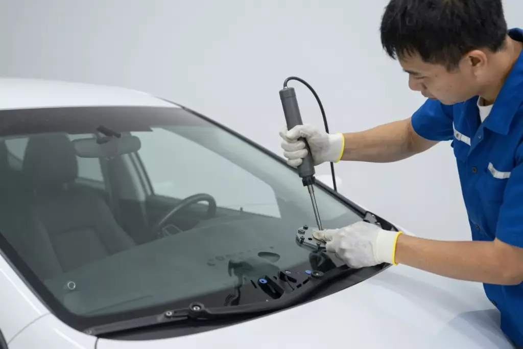A professional mechanic in a clean workshop carefully installing a new windshield into a modern Acura sedan, using specialized tools, with bright lighting and a focus on precision and quality