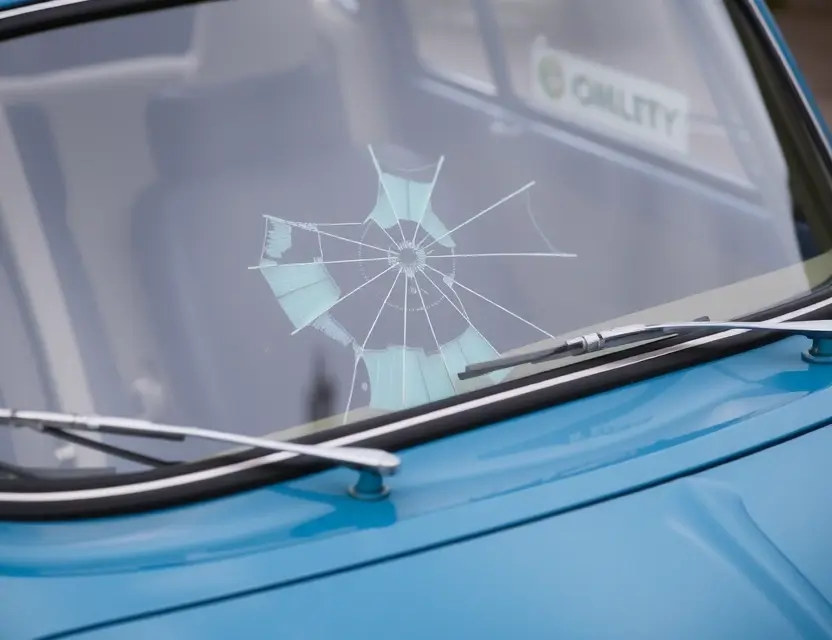 A close-up shot of an Austin 1100 car with a cracked windshield, showing the area where the windshield needs replacement. The car is parked on a clean, slightly reflective surface. Focus on the damaged windshield area.